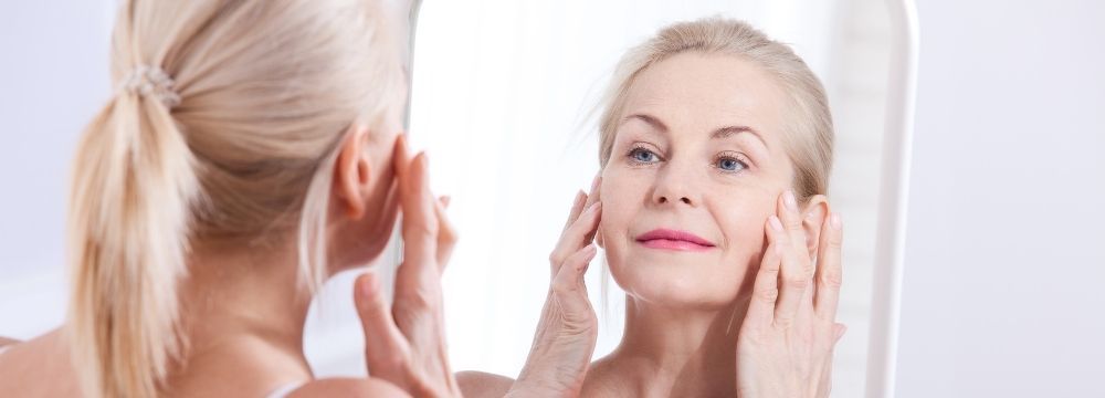 Woman examines her skin in the mirror enjoying her results of naturally improved collagen production as she ages with advice from experts from North Atlanta Dermatology 