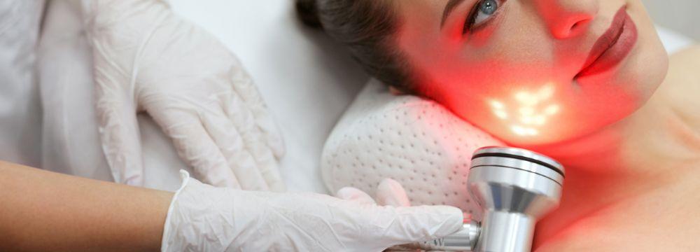 Woman receiving red light facial treatment by person wearing gloves