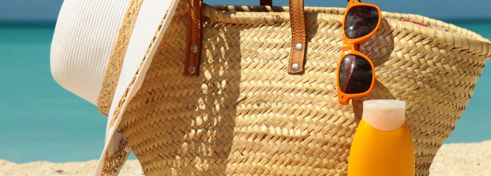 Beach bag with sunglasses and sunhat falling out next to sunscreen