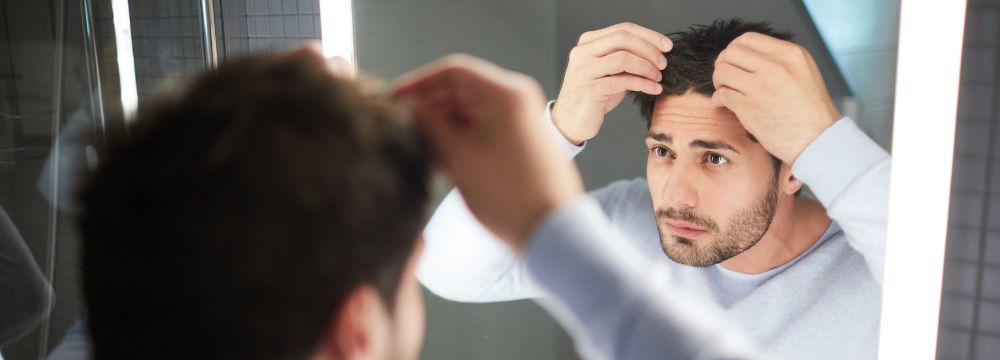 Man inspecting hair in his mirror reflection worried about hair loss