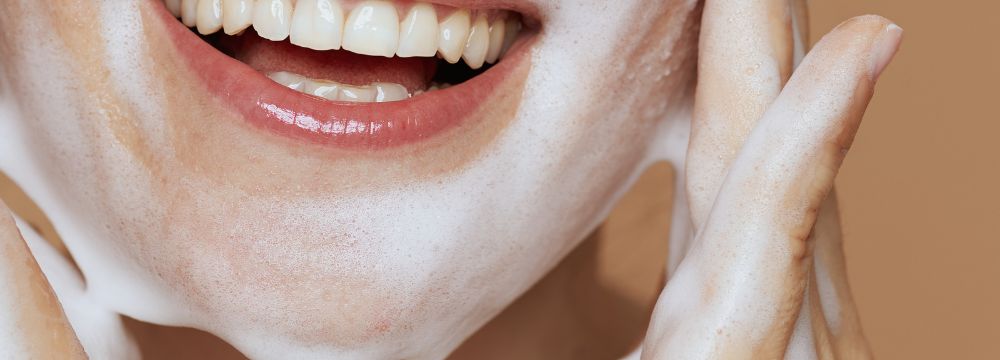 Woman smiling while washing face with foamy wash