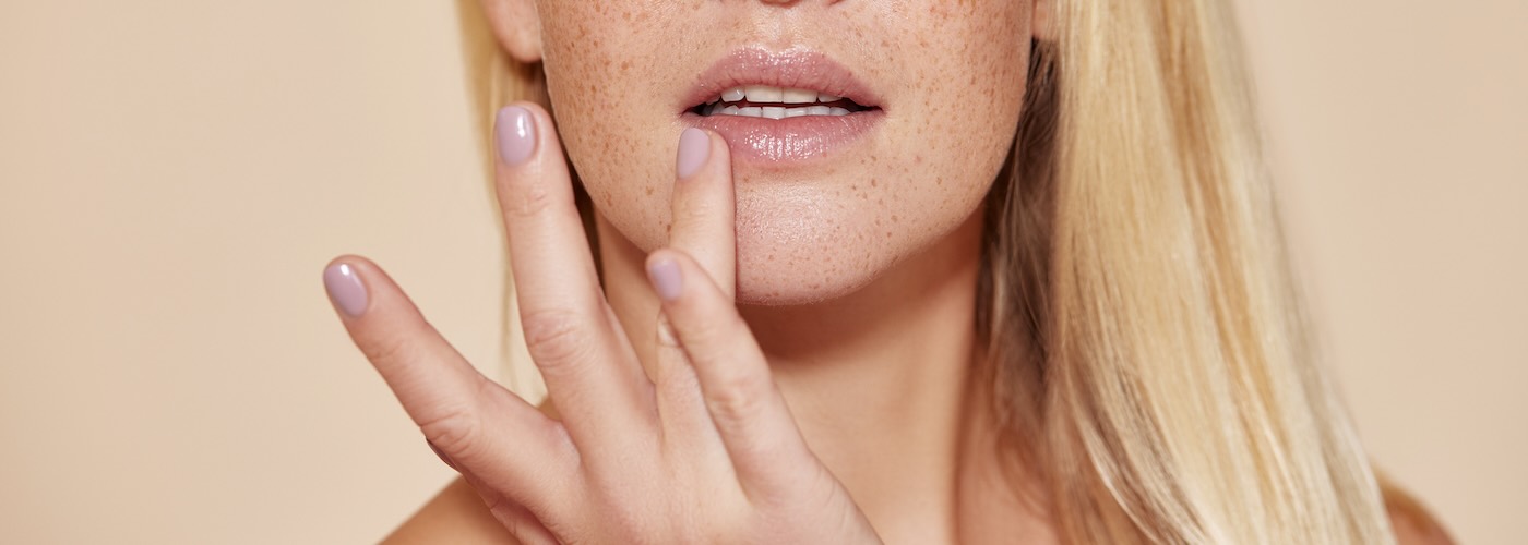 Woman with freckles touching lip with finger 