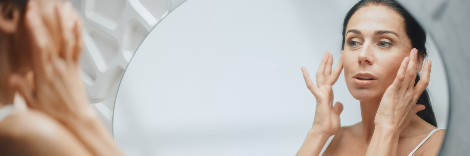 Woman checking face in mirror with both hands on face 