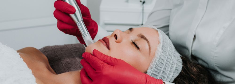 Woman lying down receiving microneedling treatment on chin by provider in red gloves 