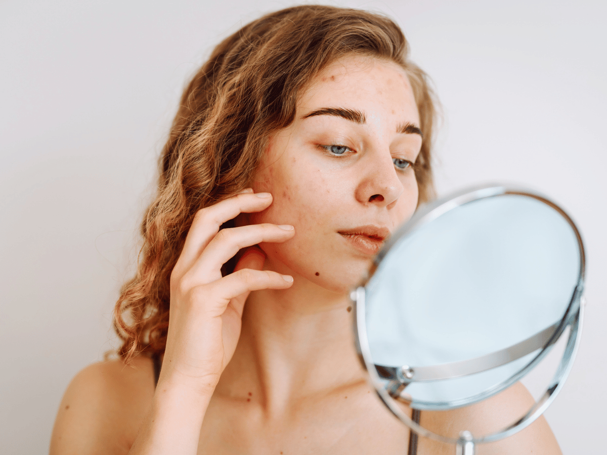 young woman using handheld mirror to examine face